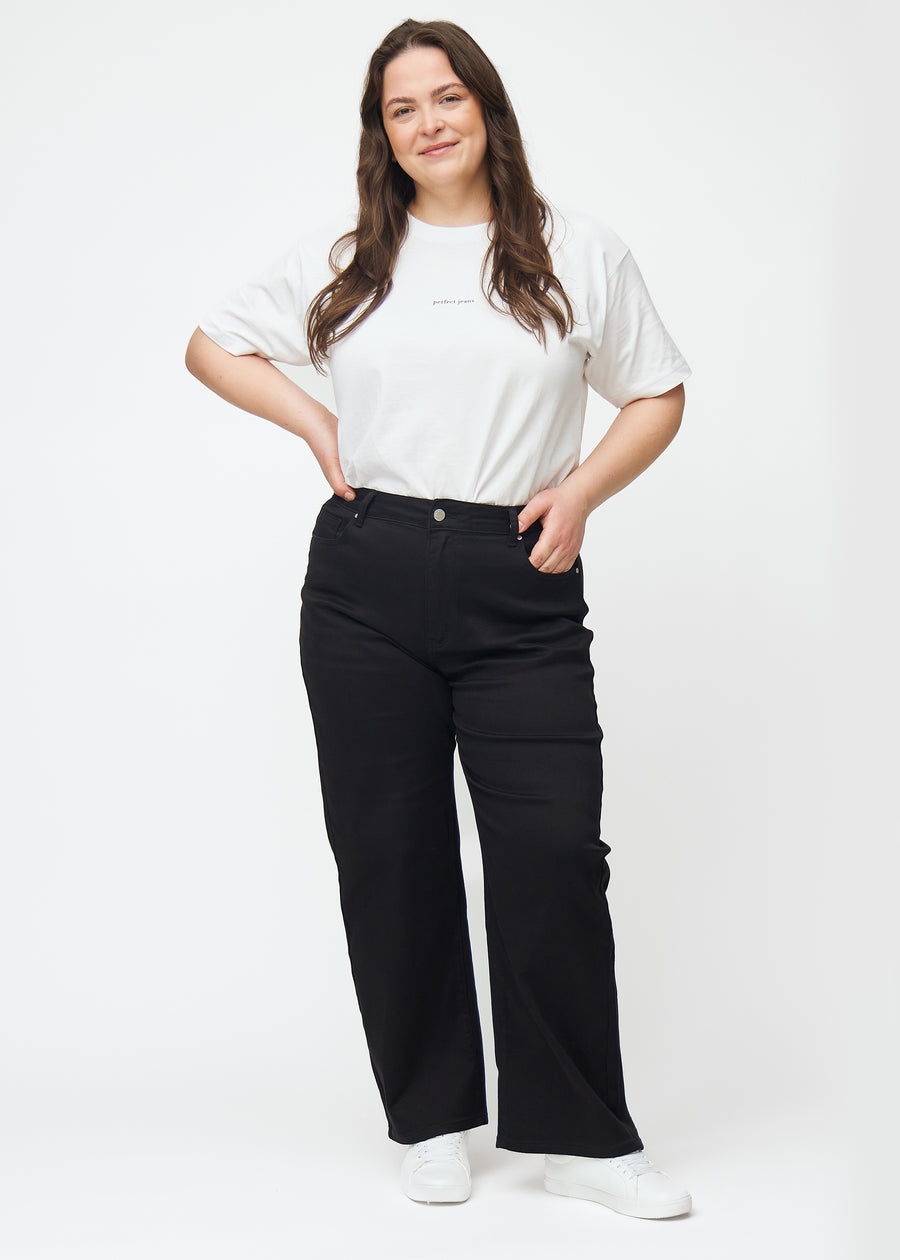 Et fuldt billede af en plus-size model i sorte højtaljede jeans, der sidder til i taljen og har en løs pasform med bredde ned.