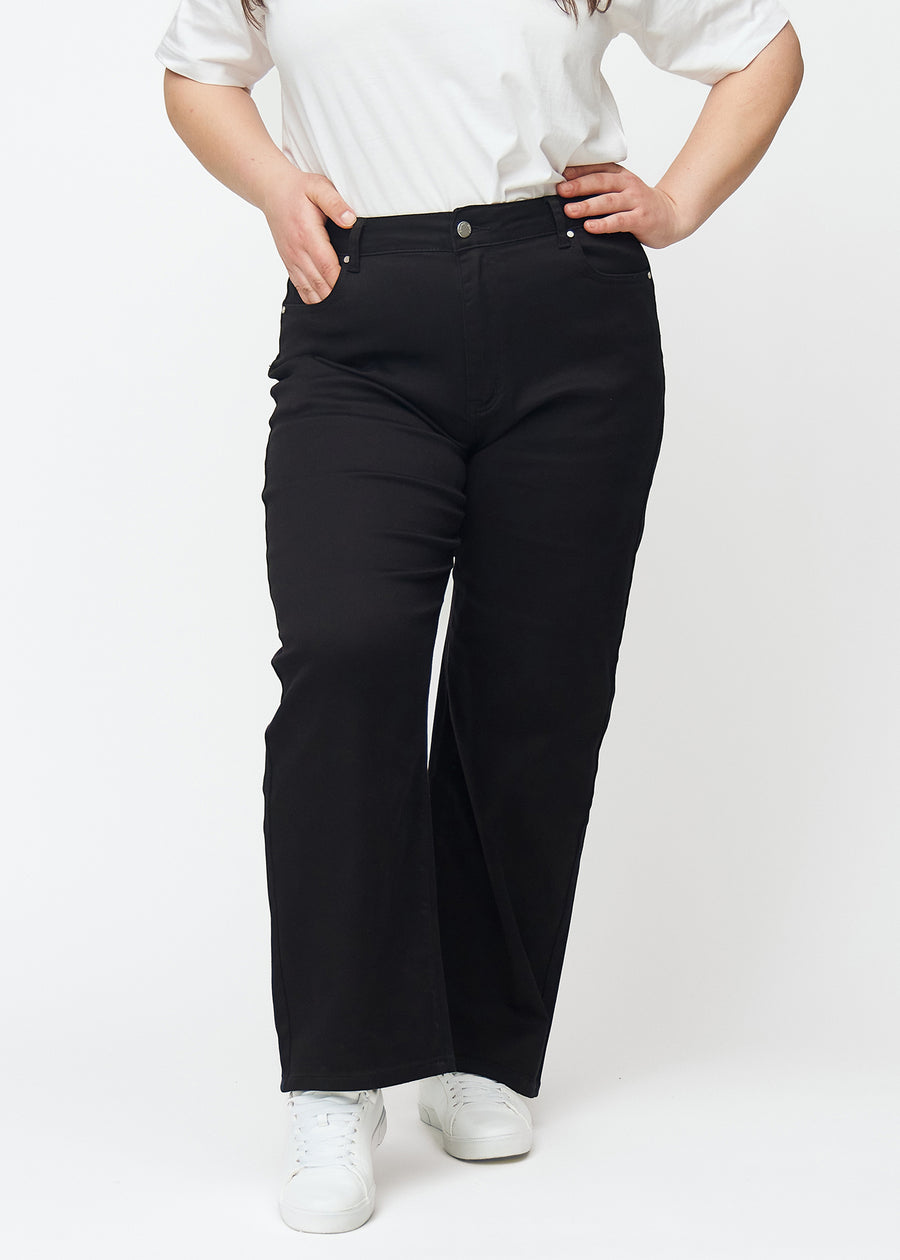 Sorte højtaljede jeans af modellen Ravens, som sidder til i taljen og har en løs pasform med bredde ned, på en plus-size model set forfra.