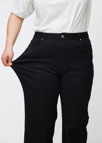 Plus-size model strækker jeansene ved låret for at vise stretch.