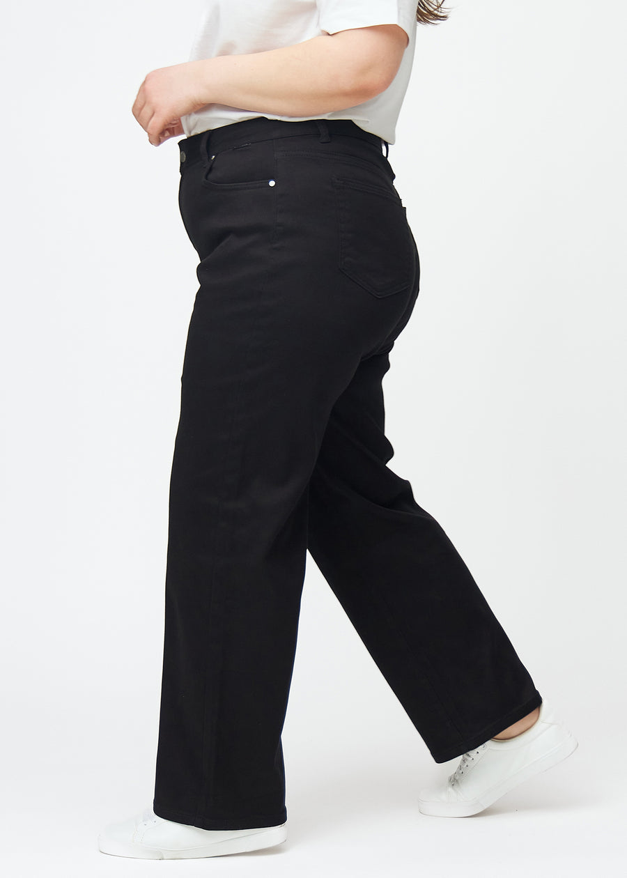 Sorte højtaljede jeans, som sidder til i taljen og har en løs pasform med bredde ned, set fra siden på en plus-size model.
