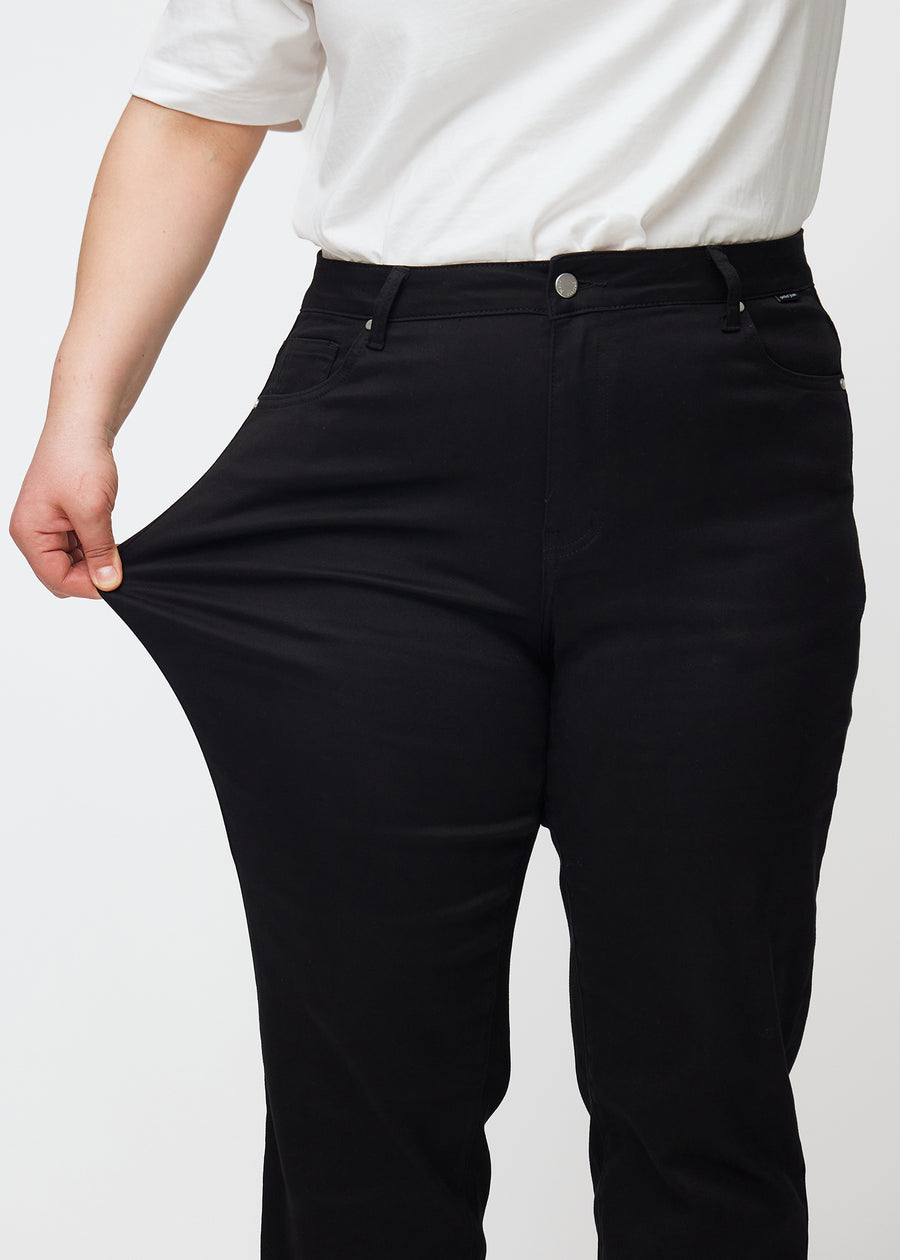 Plus-size model strækker jeansene ved låret for at vise stretch.