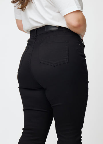 Billedet viser et nærbillede af sorte plus size high rise jeans til kvinder i farven Ravens i skinny fit set bagfra.