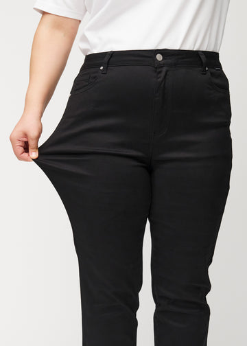 Plus-size model strækker jeansene ved låret for at vise stretch.