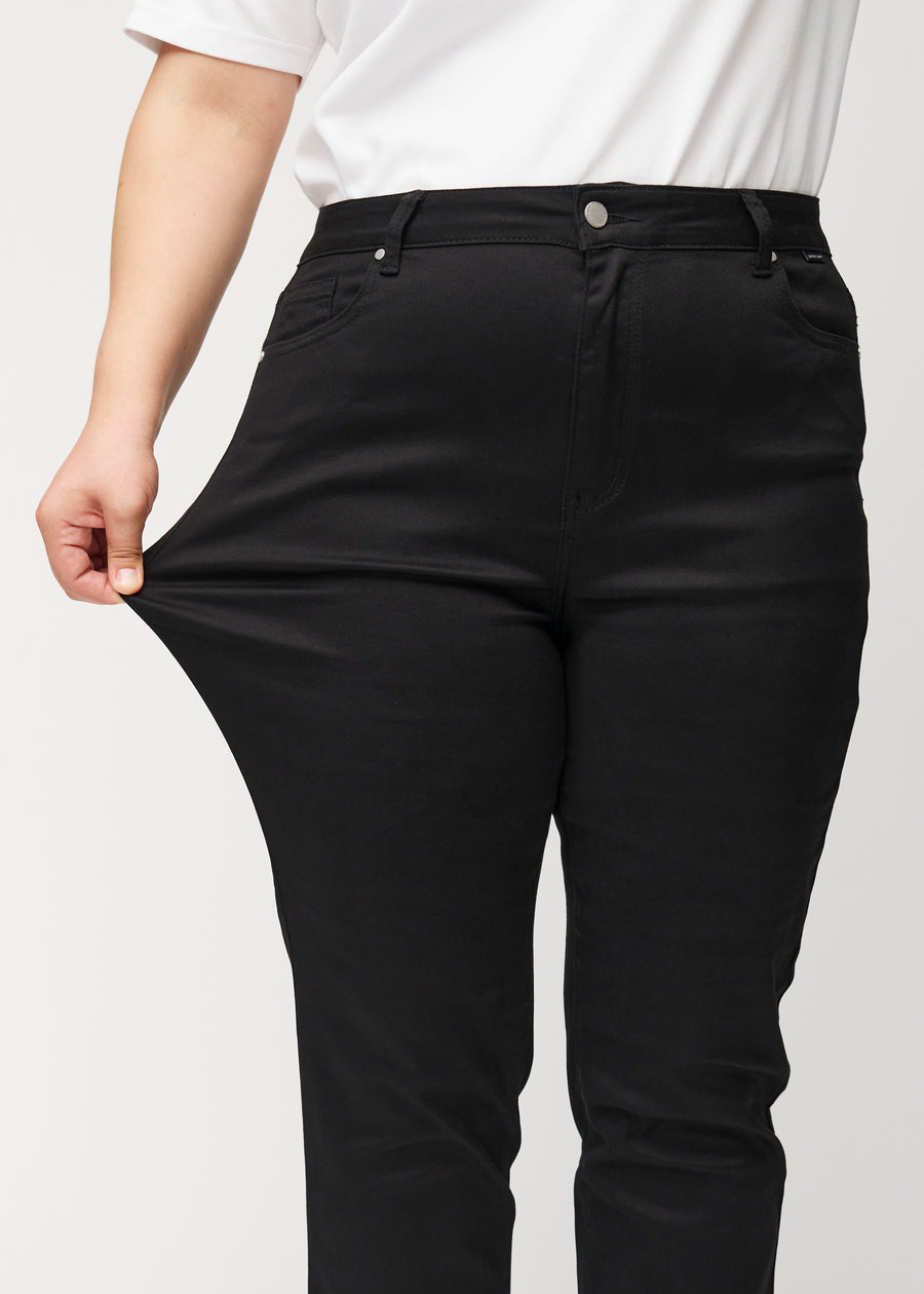Plus-size model strækker jeansene ved låret for at vise stretch.