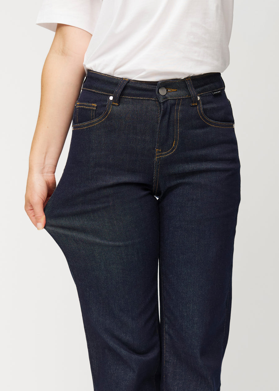 Model strækker dyb mørkeblå denim jeans til kvinder i farven Midnights ved låret for at vise materialets stretch.
