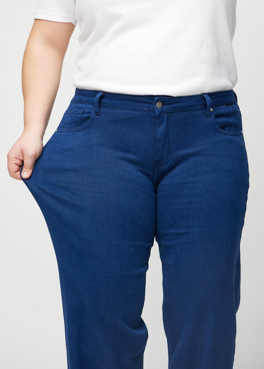 Plus-size model strækker jeansene ved låret for at vise stretch.