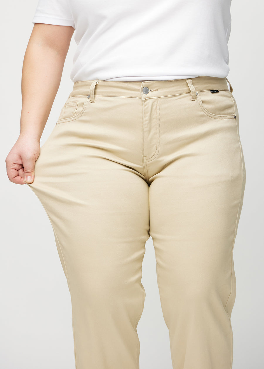 Plus-size model strækker jeansene ved låret for at vise stretch.