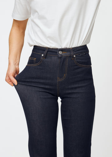 Model strækker dyb mørkeblå denim jeans til kvinder i farven Midnights ved låret for at vise materialets stretch.