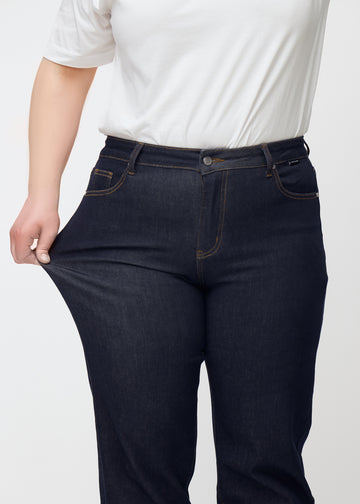 Plus-size model strækker dyb mørkeblå denim jeans til kvinder i farven Midnights ved låret for at vise materialets stretch.