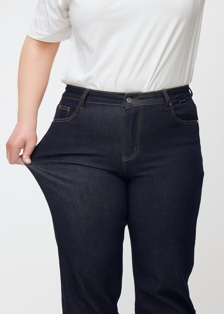 Plus-size model strækker dyb mørkeblå denim jeans til kvinder i farven Midnights ved låret for at vise materialets stretch.