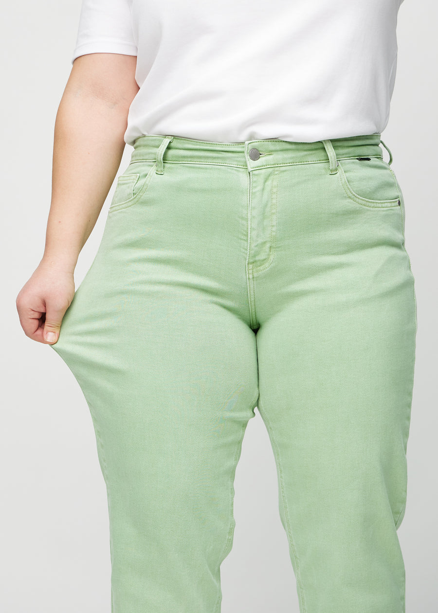 Plus-size model strækker jeansene ved låret for at vise stretch.