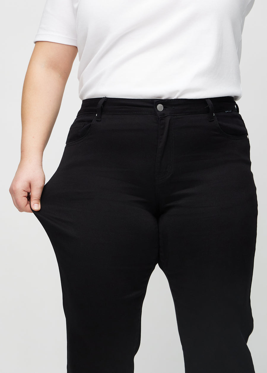 Plus-size model strækker jeansene ved låret for at vise stretch.