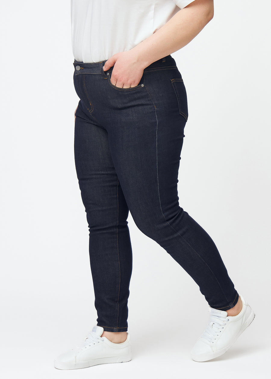 Dyb mørkeblå denim jeans til kvinder i farven Midnights med skinny pasform set fra siden på plus-size model.