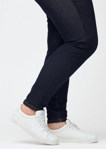 Dyb mørkeblå denim jeans til kvinder i farven Midnights med skinny pasform set tæt på ved anklerne på plus-size model for at vise den tætsiddende afslutning.