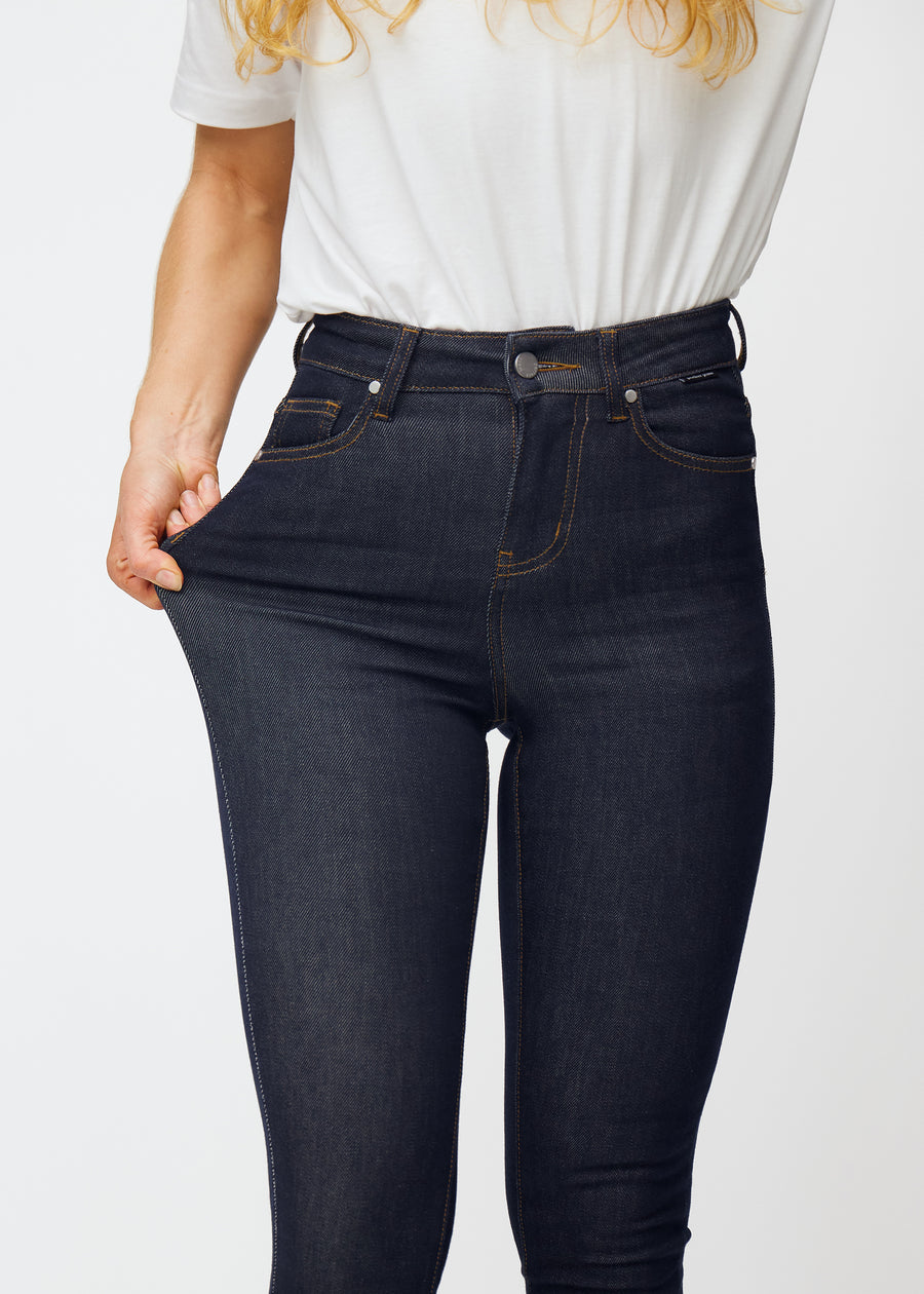 Model strækker dyb mørkeblå denim jeans til kvinder i farven Midnights ved låret for at vise materialets stretch.