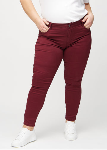 Mørkerøde skinny jeans, modelnavn Santas, som sidder tæt til benet på en plus-size model, set forfra.