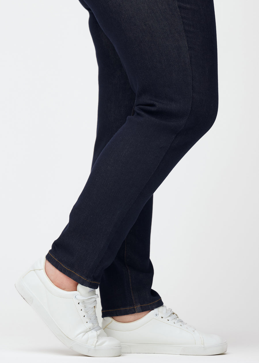 Dyb mørkeblå denim jeans til kvinder i farven Midnights med slim pasform set tæt på ved anklerne på plus-size model for at vise den figursyede afslutning.