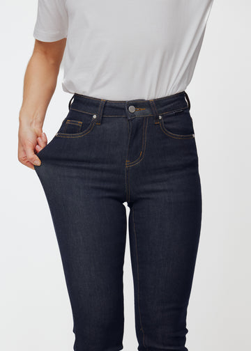 Model strækker dyb mørkeblå denim jeans til kvinder i farven Midnights ved låret for at vise materialets stretch.