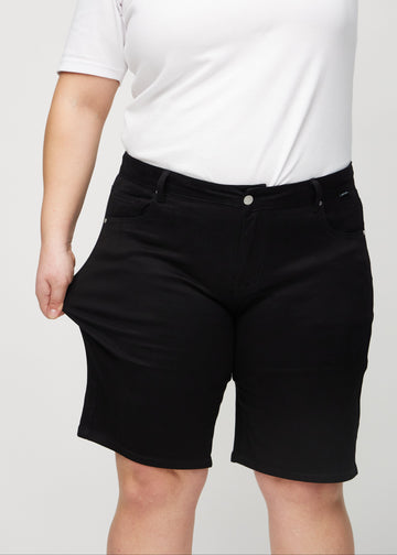 Plus-size model strækker shortsene ved låret for at vise stretch.