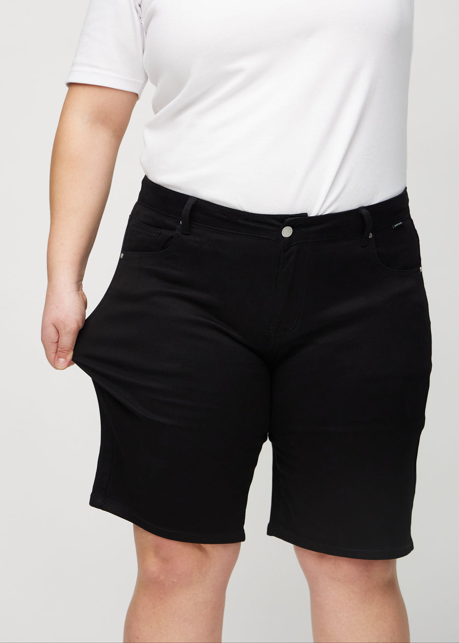 Plus-size model strækker shortsene ved låret for at vise stretch.