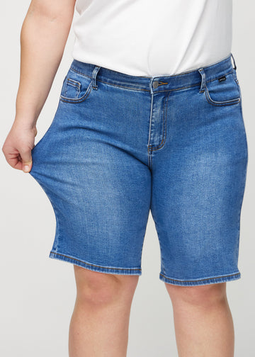 Plus-size model strækker shortsene ved låret for at vise stretch.