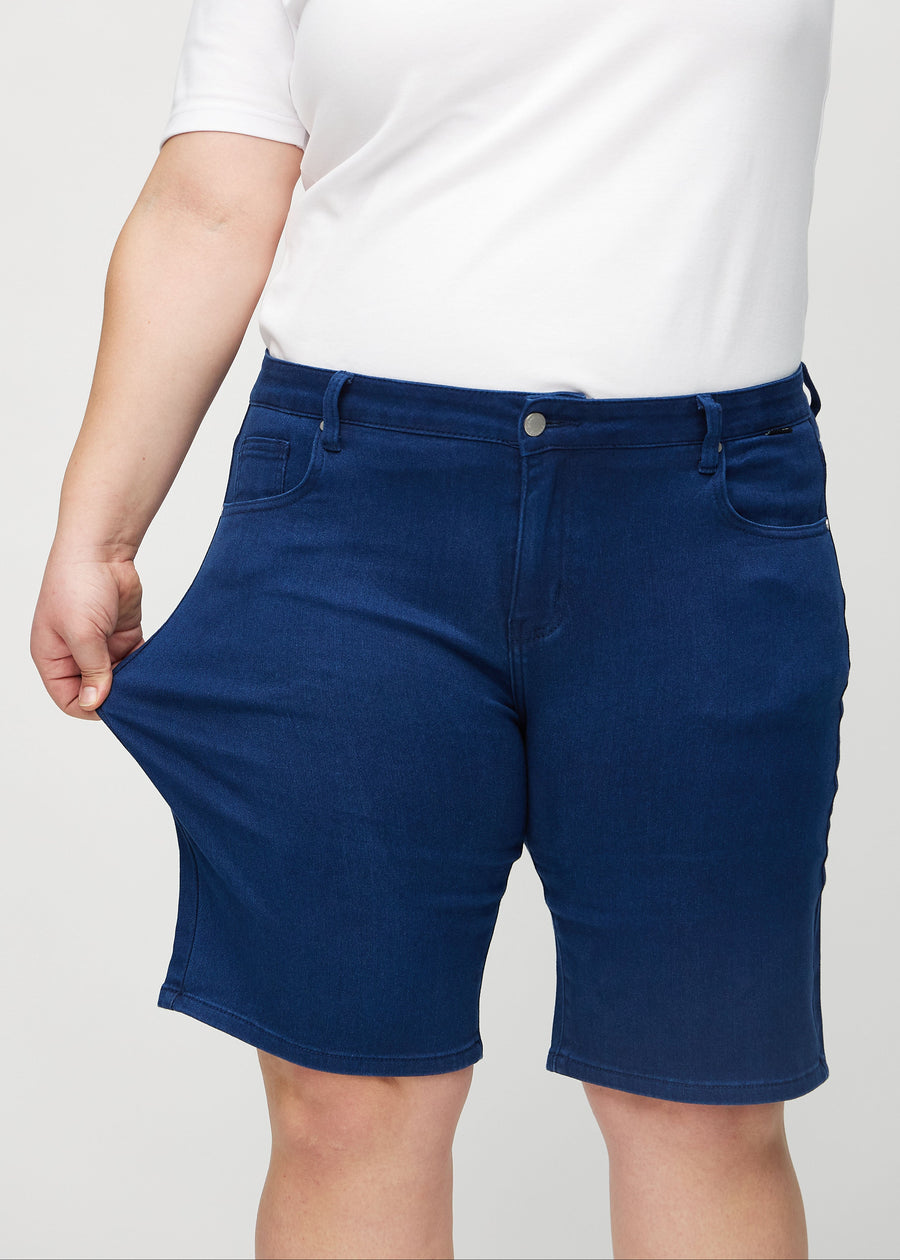 Plus-size model strækker shortsene ved låret for at vise stretch.
