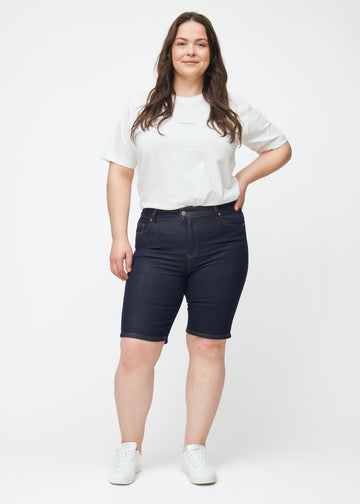 Fuldt billede af plus-size model i dyb mørkeblå denim shorts til kvinder i farven Midnights med skinny pasform.