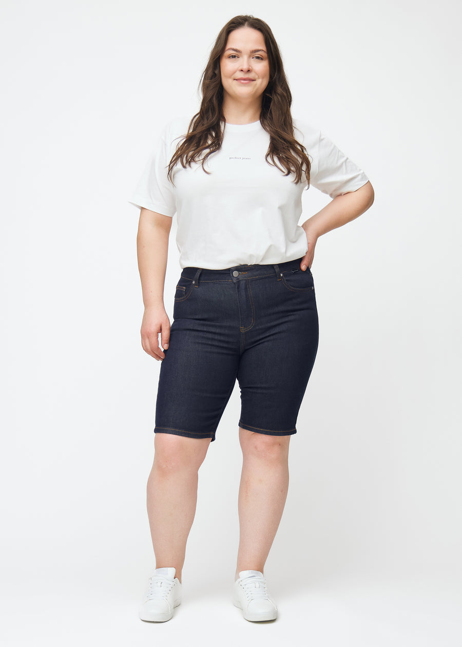 Fuldt billede af plus-size model i dyb mørkeblå denim shorts til kvinder i farven Midnights med skinny pasform.