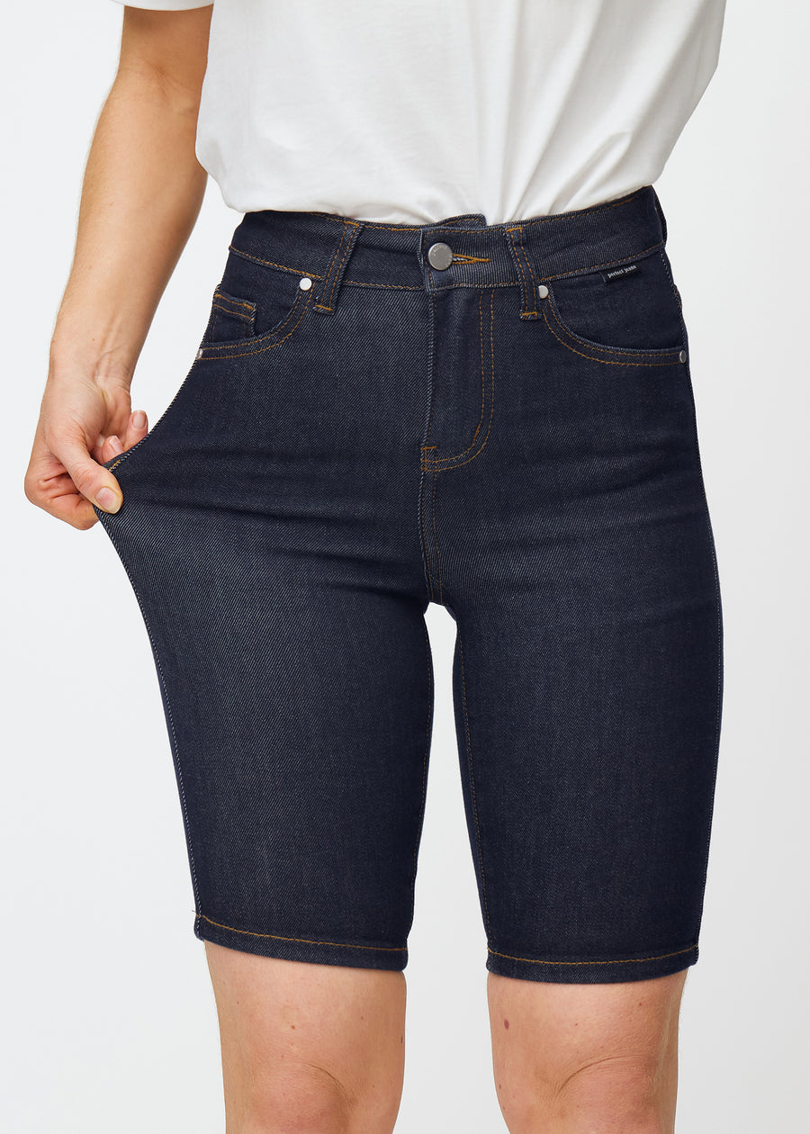 Model strækker dyb mørkeblå denim shorts til kvinder i farven Midnights ved låret for at vise materialets stretch.