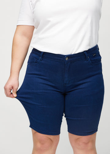 Plus-size model strækker shortsene ved låret for at vise stretch.