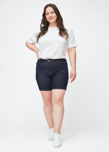 Fuldt billede af plus-size model i dyb mørkeblå denim shorts til kvinder i farven Midnights med skinny pasform.