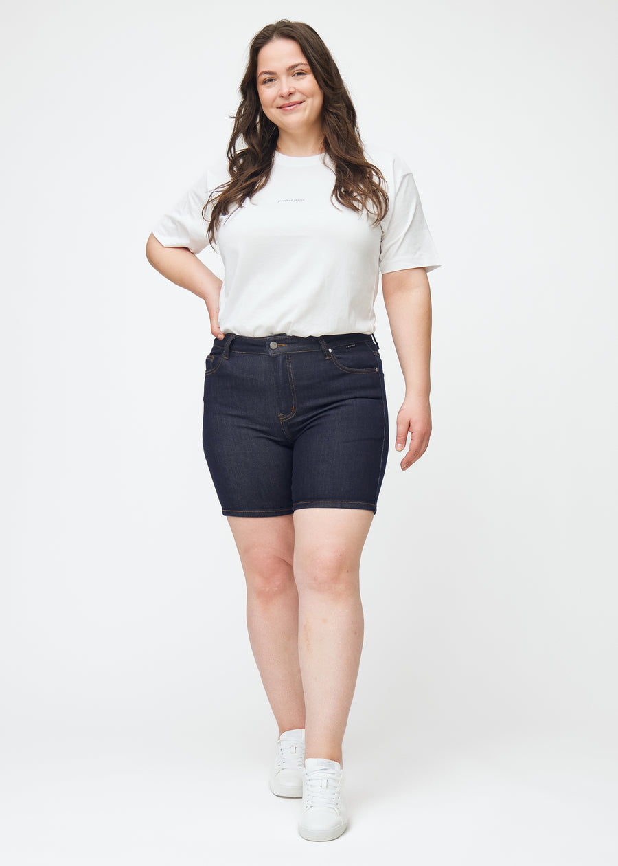 Fuldt billede af plus-size model i dyb mørkeblå denim shorts til kvinder i farven Midnights med skinny pasform.