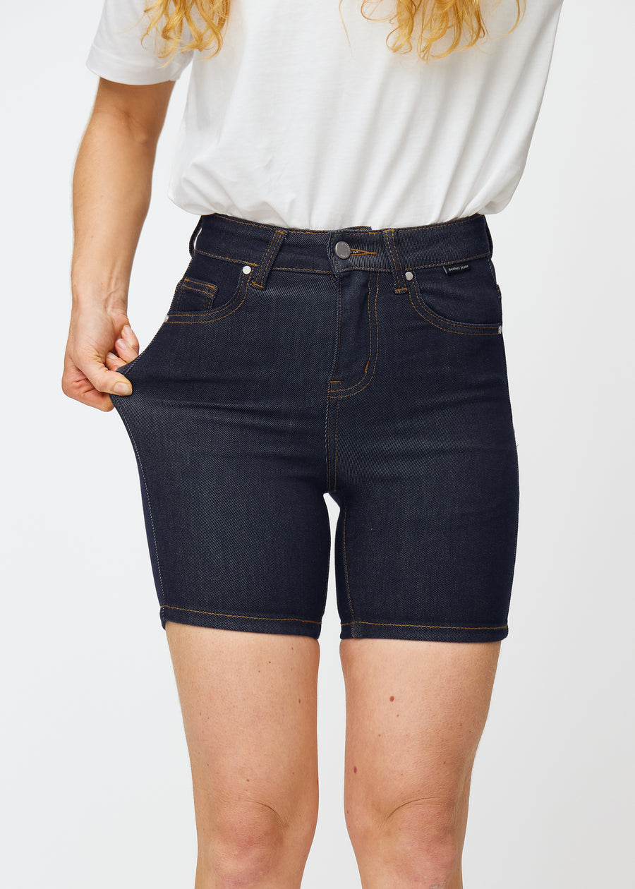 Model strækker dyb mørkeblå denim shorts til kvinder i farven Midnights ved låret for at vise materialets stretch.