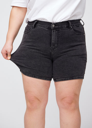 Plus-size model strækker shortsene ved låret for at vise stretch.