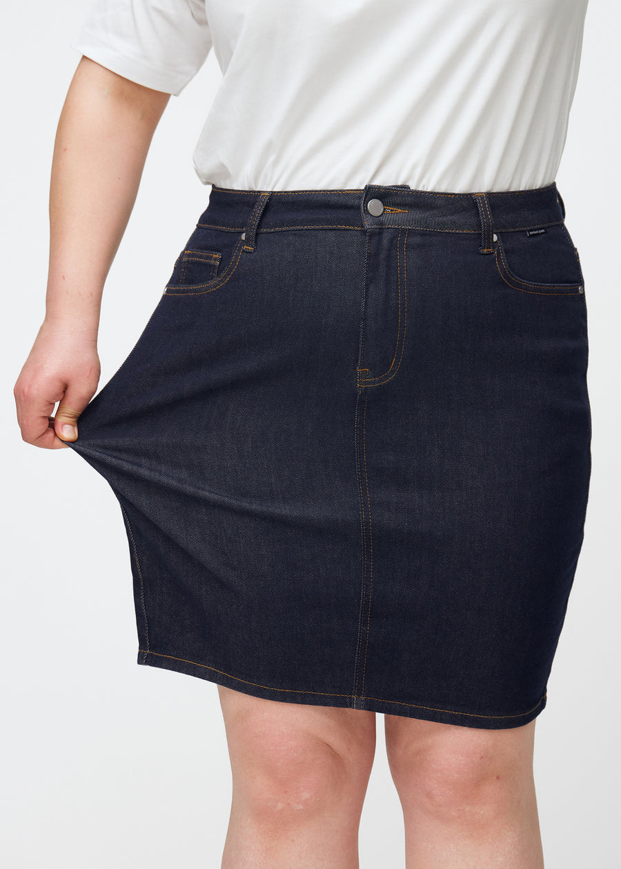 Plus-size model strækker dyb mørkeblå denim nederdel til kvinder i farven Midnights ved låret for at vise materialets stretch.