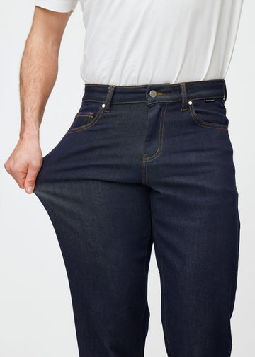 Model strækker dyb mørkeblå denim jeans til mænd i farven Midnights ved låret for at vise materialets stretch.