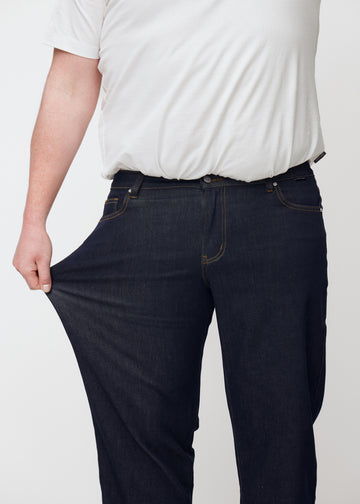 Plus-size model strækker dyb mørkeblå denim jeans til mænd i farven Midnights ved låret for at vise materialets stretch.