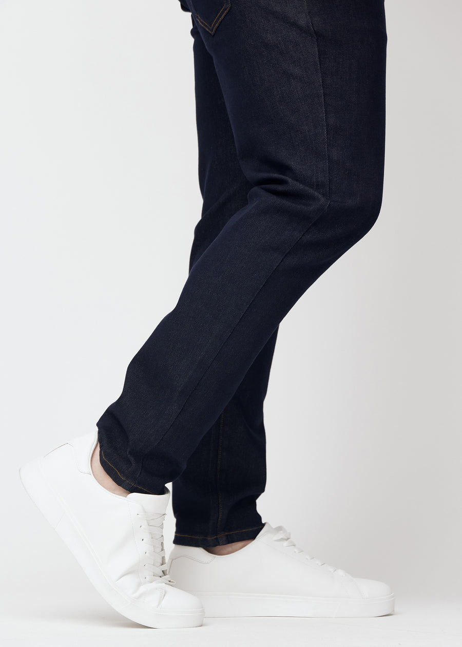 Dyb mørkeblå denim jeans til mænd i farven Midnights med slim pasform set tæt på ved anklerne på plus-size model for at vise den smalle afslutning.