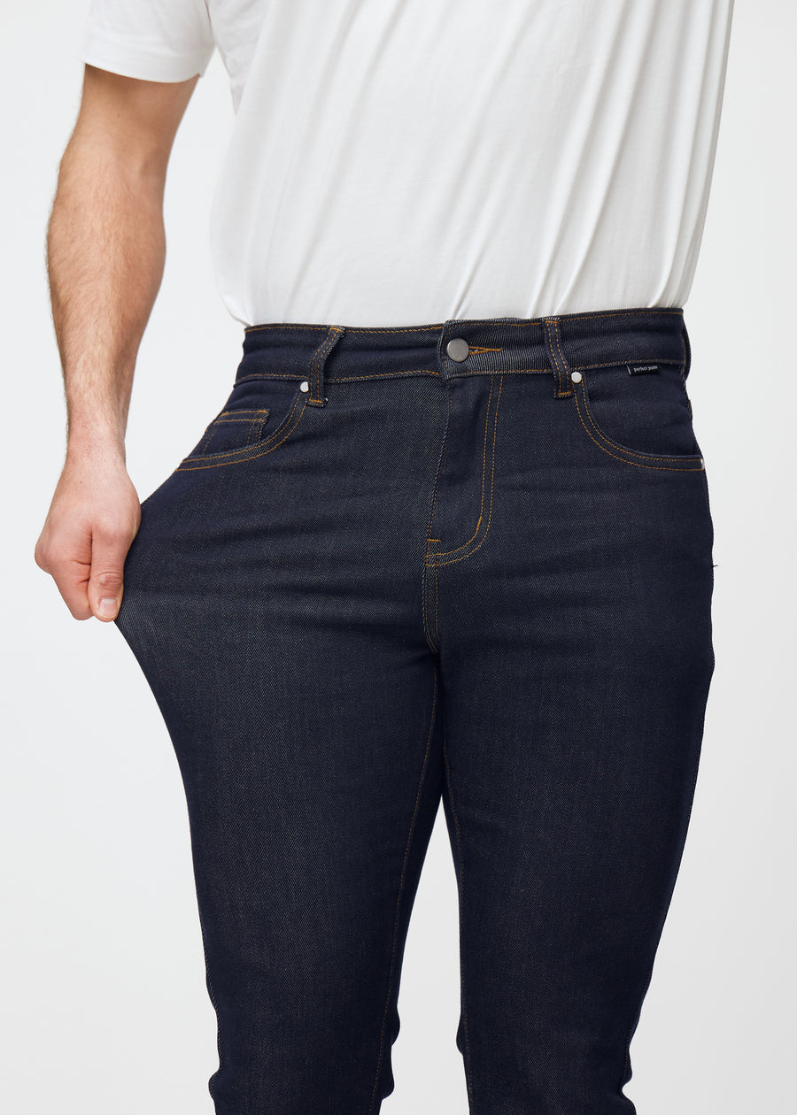 Model strækker dyb mørkeblå denim jeans til mænd i farven Midnights ved låret for at vise materialets stretch.