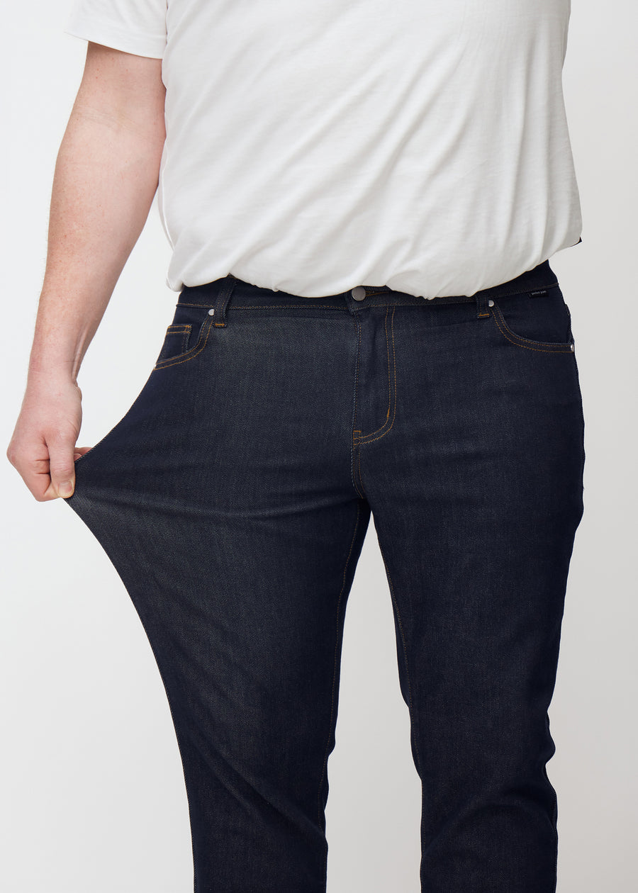 Plus-size model strækker dyb mørkeblå denim jeans til mænd i farven Midnights ved låret for at vise materialets stretch.