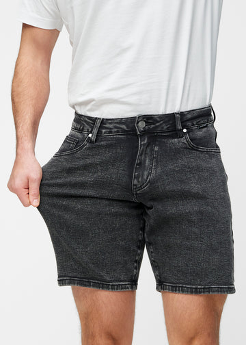 Model strækker mørkegrå denim shorts til mænd i farven Shadows ved låret for at vise materialets stretch.