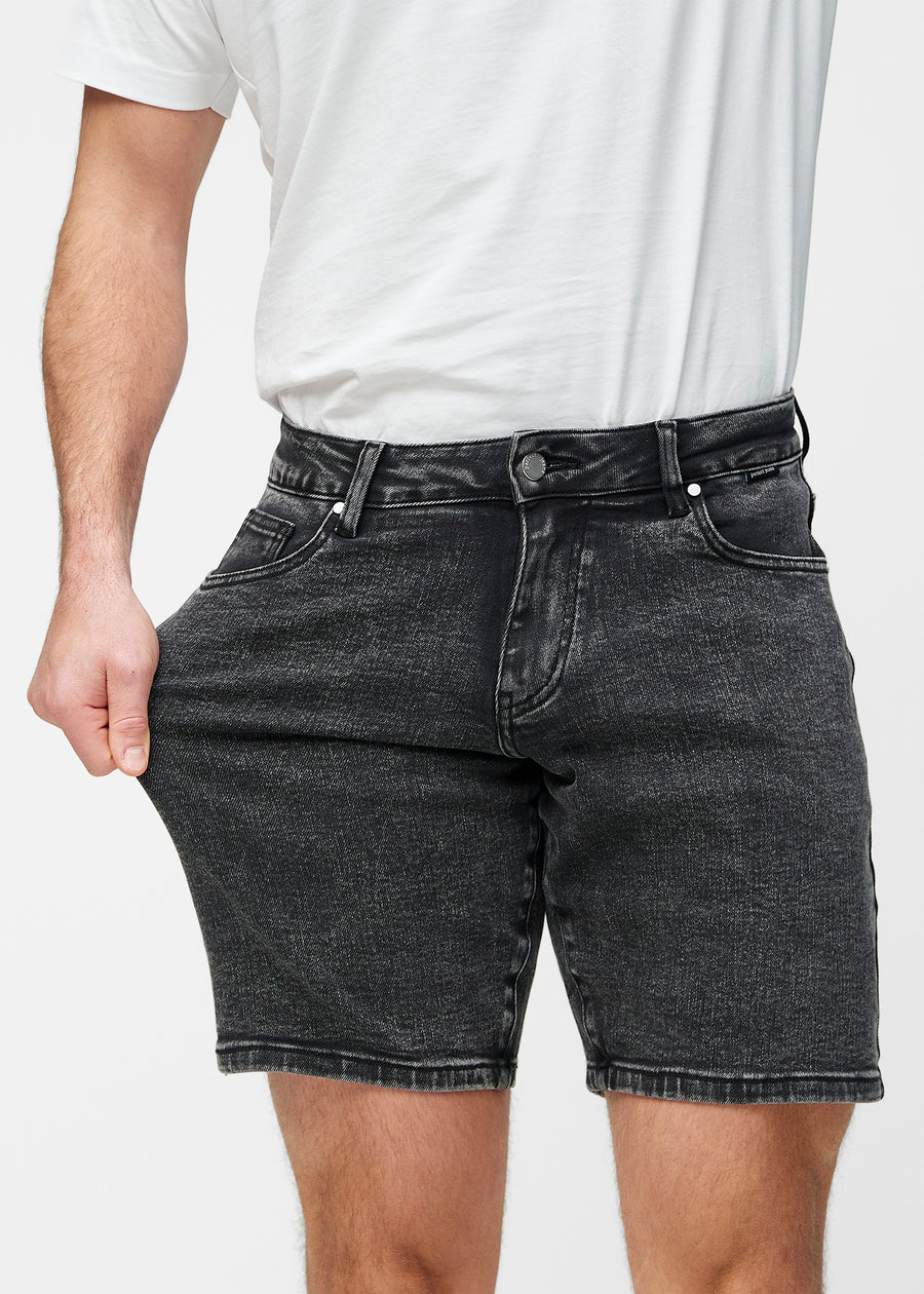 Model strækker mørkegrå denim shorts til mænd i farven Shadows ved låret for at vise materialets stretch.