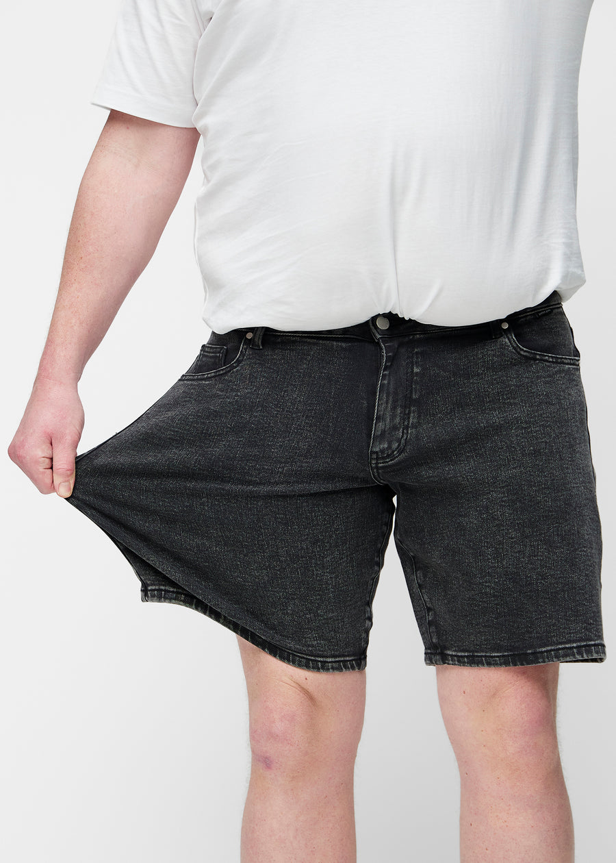 Plus-size model strækker mørkegrå denim shorts til mænd i farven Shadows ved låret for at vise materialets stretch.