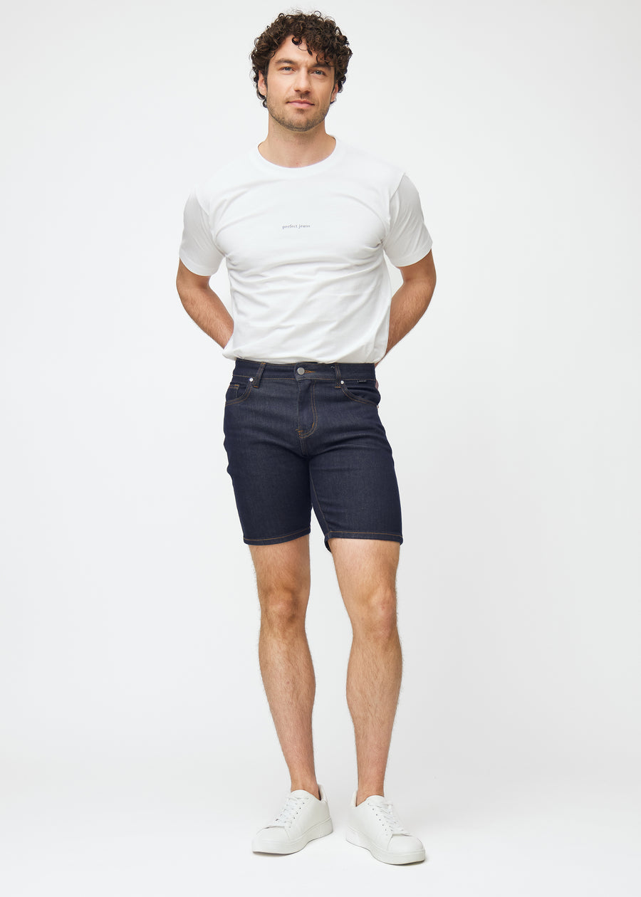 Fuldt billede af model i dyb mørkeblå denim shorts til mænd i farven Midnights med slim pasform.