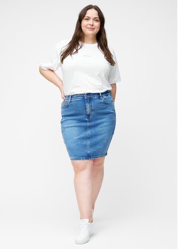 Plus-size model viser klassisk blå, tætsiddende og knælang denimnederdel i bevægelse og strækker materialet.
