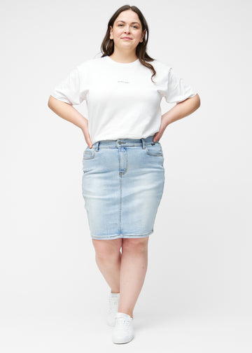 Plus-size model viser lyseblå, tætsiddende og knælang denimnederdel i bevægelse og strækker materialet.
