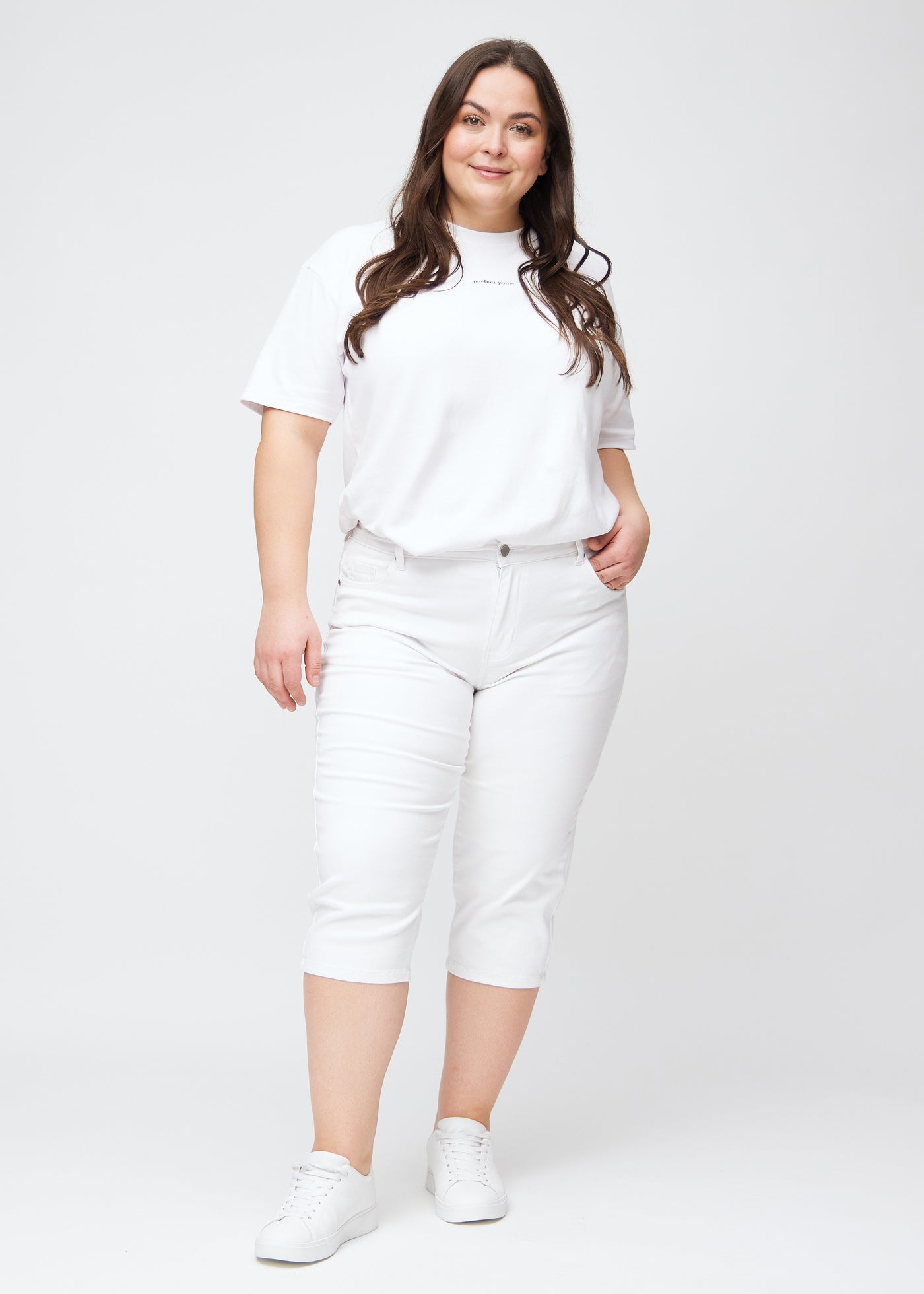 Plus-size model går ind i billedet, strækker i sine hvide slim capris, drejer rundt for at vise dem frem og forlader derefter billedet.